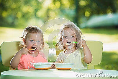 Two little girls sitting at a table and eating together against green lawn Stock Photo