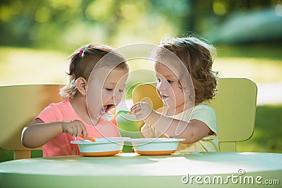 Two little girls sitting at a table and eating together against green lawn Stock Photo