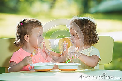 Two little girls sitting at a table and eating together against green lawn Stock Photo