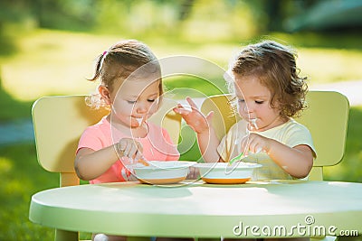 Two little girls sitting at a table and eating together against green lawn Stock Photo