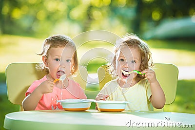 Two little girls sitting at a table and eating together against green lawn Stock Photo