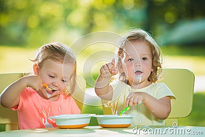 Two little girls sitting at a table and eating together against green lawn Stock Photo