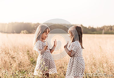 Two little happy identical twin girls playing together in nature in summer. Girls friendship and youth concept. Active children`s Stock Photo