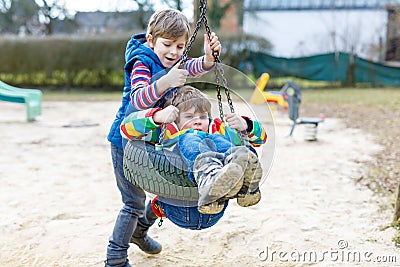 Two little kid boys having fun with chain swing on outdoor playground Stock Photo