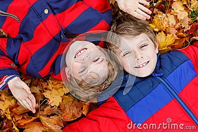 Two little kid boys lying in autumn leaves in colorful fashion fall clothing. Stock Photo