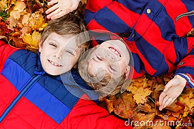 Two little kid boys lying in autumn leaves in colorful fashion fall clothing. Stock Photo