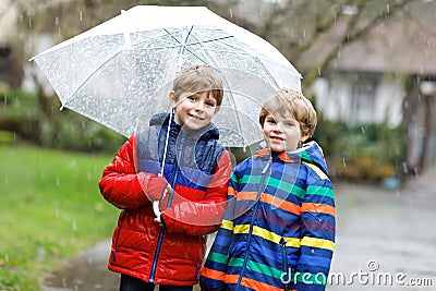 Two little kid boys on way to school walking during sleet, rain and snow with an umbrella on cold day Stock Photo