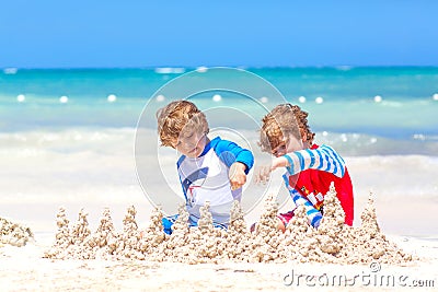 Two little kids boys having fun with building a sand castle on tropical beach on island. Healthy children playing Stock Photo