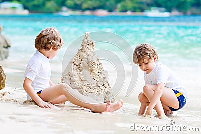 Two little kids boys having fun with building a sand castle on tropical beach of Seychelles. children playing together Stock Photo