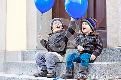 Two little kids boys playing with blue air balloons outdoors. Happy twins and toddler brothers smiling and laughing Stock Photo