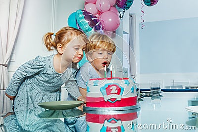 Two little kids girl and a boy blow candles on the birthday cake Stock Photo