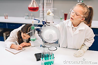 Two little kids in lab coat learning chemistry in school laboratory. Young scientists in protective glasses making Stock Photo