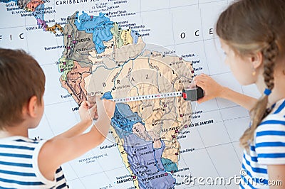 Two little kids in striped shirt measuring with tape world map during geography education Stock Photo