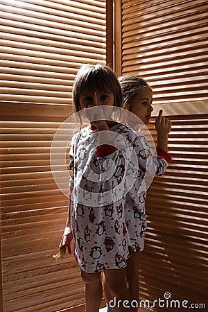 Two little sisters dressed in the pajamas are hiding in the closet with wooden doors Stock Photo