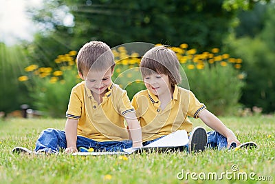 Two little sweet boys, brothers, reading a book in the park Stock Photo