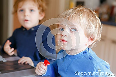 Two little toddler boys, cute brother children watching cartoons on tv and eating lolipop candy. Happy siblings together Stock Photo