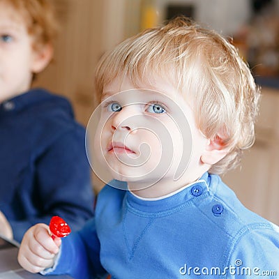 Two little toddler boys, cute brother children watching cartoons on tv and eating lolipop candy. Happy siblings together Stock Photo