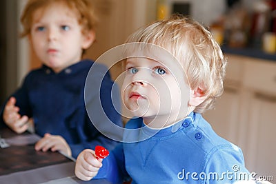 Two little toddler boys, cute brother children watching cartoons on tv and eating lolipop candy. Happy siblings together Stock Photo