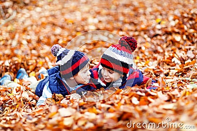 Two little twin boys lying in autumn leaves in colorful clothing. Happy siblings kids having fun in autumn forest or Stock Photo