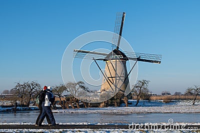 Two locals on a frozen windmill canal pathway at sunrise moment Stock Photo