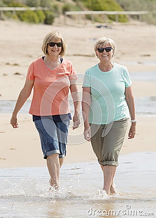 Two lovely senior mature retired women on their 60s having fun enjoying together happy walking on the beach smiling playful Stock Photo