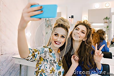 Two lovely smiled young women having fun, making selfie on phone in hairdresser salon. Smiling, expressing positivity Stock Photo