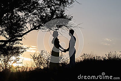 Two lovers girl and a man stand under a beautiful tree in the rays of the sunset in the evening of summer. Beautiful romantic Stock Photo