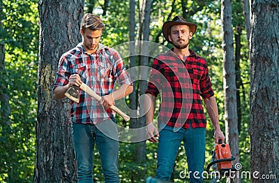 Two lumberjacks with chainsaw and axe. Male lumberjack in the forest. Woodcutter with axe and lumberjack with chainsaw. Stock Photo