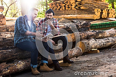 two lumberjacks sitting on logs with axe and using digital tablet Stock Photo