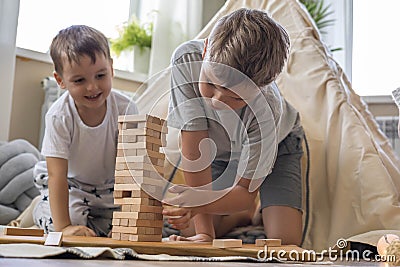 Two male children playing Jenga hardwood bricks tower construction childish room with linen wigwam Stock Photo