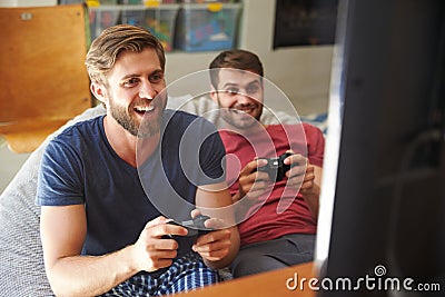 Two Male Friends In Pajamas Playing Video Game Together Stock Photo