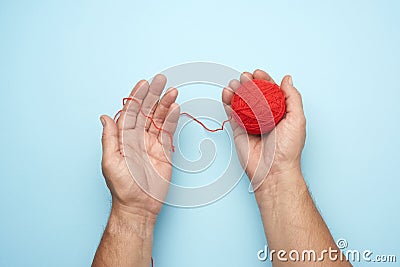 Two male hands hold a ball of red woolen threads, blue background Stock Photo