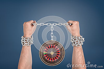 Two male hands trying to break a chain binding them and connected to a small roulette wheel. Stock Photo