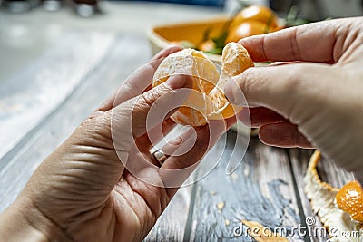 two man's hands separating a segment of ripe tangerine and in the background a basket Stock Photo