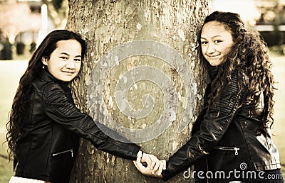 Two Maori sisters holding hands hugging a tree Stock Photo