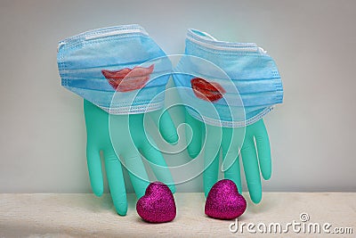 Two medical masks with painted red lips are worn on surgical gloves. Next to two scarlet hearts Stock Photo