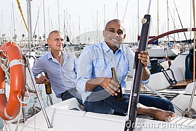 Two men in blue shirts relaxing on sailing yacht in the port Stock Photo