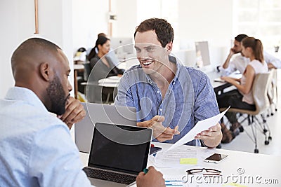 Two men discussing business documents in a busy office Stock Photo