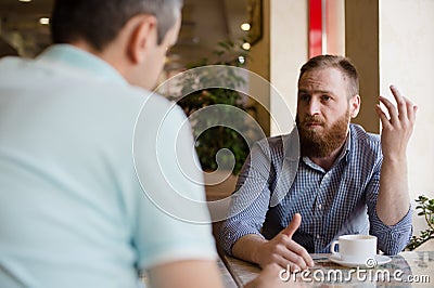 Two men discussing difficult issues with emotions during coffee break in cafe talking about problems of business negotiation Stock Photo