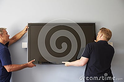 Two Men Fitting Flat Screen Television To Wall Stock Photo