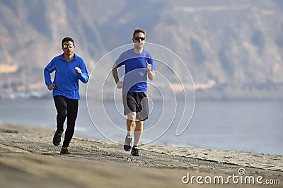 Two men friends running together on beach sand coast mountain bachground in healthy lifestyle concept Stock Photo