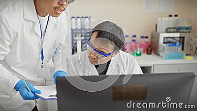 Two men in lab coats using computer in a science laboratory environment Stock Photo