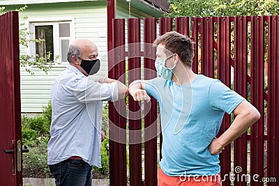 Two men in medical mask greeting each other with elbows on sunny day Stock Photo