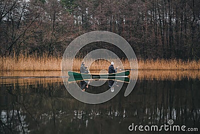 Two men paddling a beautiful green canoe on the river. Spring or autumn scene with a wooden boat on calm water Stock Photo