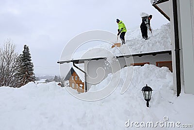 Two men shoveling high, heavy snow from a house roof Stock Photo