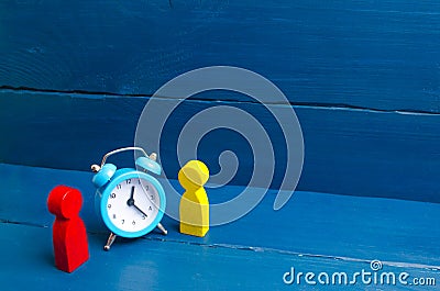 Two men stand near the blue alarm clock and talk. The concept of waiting for a meeting, a date. Punctuality. The cost of hourly Stock Photo