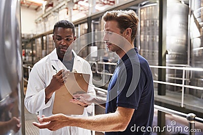 Two men talk and inspect vats in a modern winemaking factory Stock Photo