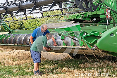 Two men undertaking basic maintenance on a stationary combine harvester. UK Editorial Stock Photo