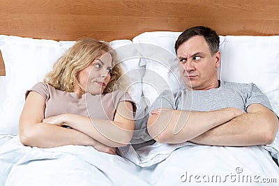 Two, a man and a woman lie on the bed and look at each other with displeasure. Relationship concept Stock Photo