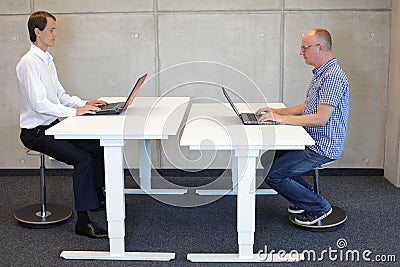 Two men working in correct sitting posture on pneumatic leaning seats Stock Photo